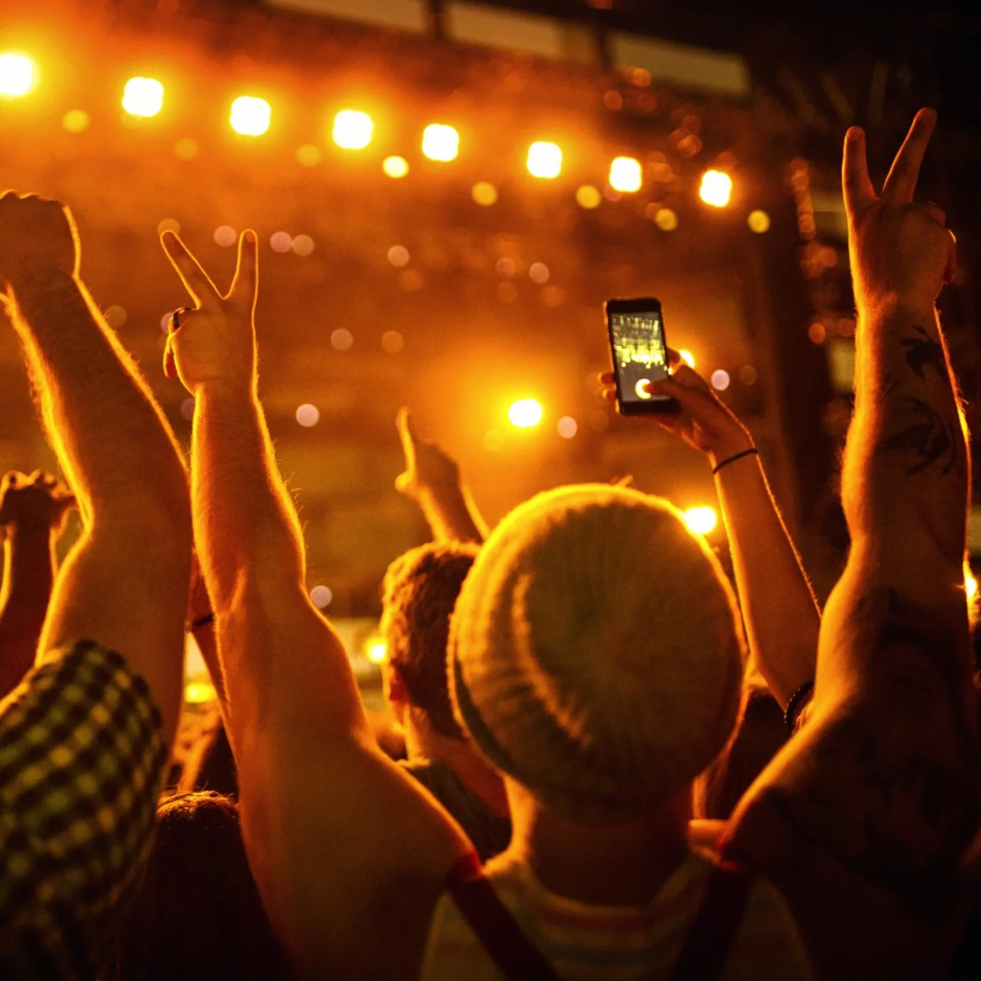 Concert crowd with raised hands, one fan filming the stage on a smartphone