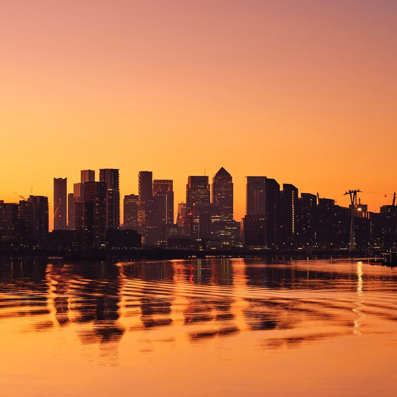 City skyline silhouetted at sunset, reflected in a river